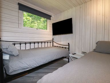 A bedroom with two single beds a wall-mounted TV and a window with a view of trees at Villa 18 Lanteglos Holiday Park near Camelford