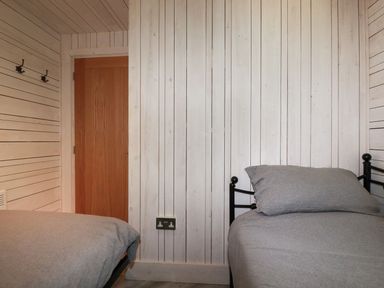 A bedroom with two single beds with grey bedding a wooden door and white wood panel walls at Villa 18 Lanteglos Holiday Park in Lanteglos Holiday Park near Camelford