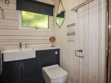 A bathroom with a white sink and toilet dark cabinets window with a black blind and a heart shaped mirror at Villa 18 Lanteglos Holiday Park near Camelford