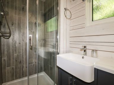 A bathroom with a shower enclosure with glass doors a sink on a cabinet and a frosted window at Villa 18 Lanteglos Holiday Park near Camelford