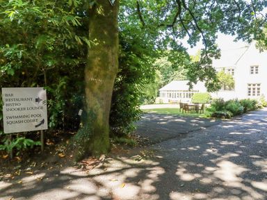 An outdoor area with a large tree and a signpost showing directions to a bar restaurant bistro snooker lounge swimming pool and squash court at Villa 18 Lanteglos Holiday Park near Camelford