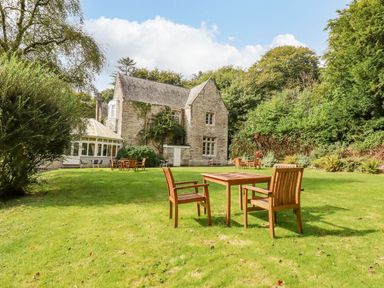 A garden with wooden tables and chairs near a stone building with large windows at Villa 18 Lanteglos Holiday Park in Lanteglos Holiday Park near Camelford