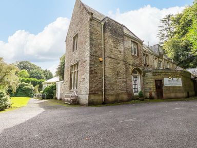 An exterior view of a stone building with a driveway and outdoor seating at Lanteglos Holiday Park near Camelford