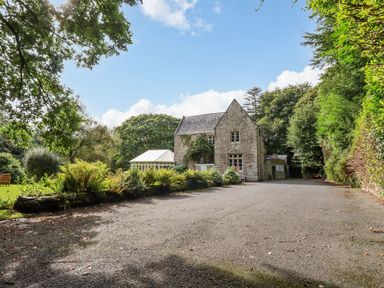 A stone house with a paved driveway surrounded by trees and shrubs at Villa 18 Lanteglos Holiday Park near Camelford