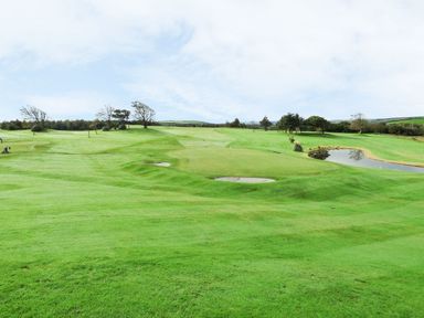 A golf course with green grass sand traps trees and a small water hazard at Villa 18 Lanteglos Holiday Park near Camelford