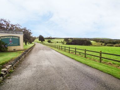 A paved road with a fence alongside green fields and a sign for Bowood Park and Golf Course