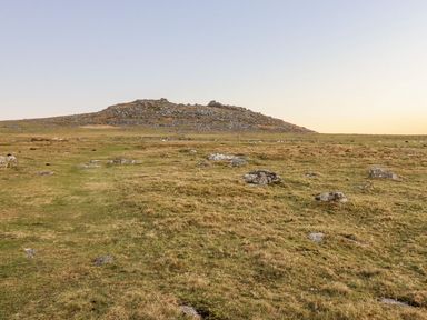 A grassy moorland with scattered rocks and a low rocky hill under a clear sky at Villa 18 Lanteglos Holiday Park near Camelford