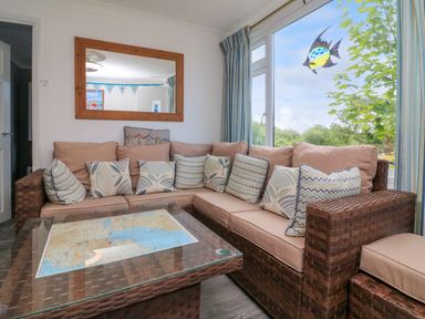 A seating area with a wicker sofa and a glass coffee table with a map underneath near a large window at 4 The Park in Kilkhampton