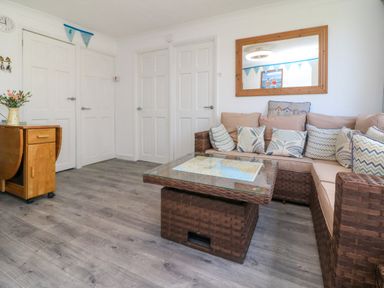 A living room with a wicker corner sofa and glass coffee table near white doors at 4 The Park in Kilkhampton