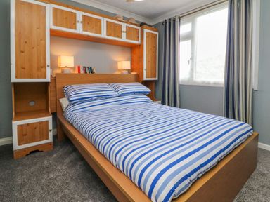 A bedroom with a wooden bed frame and built-in cupboards above and around the bed at 4 The Park in Kilkhampton