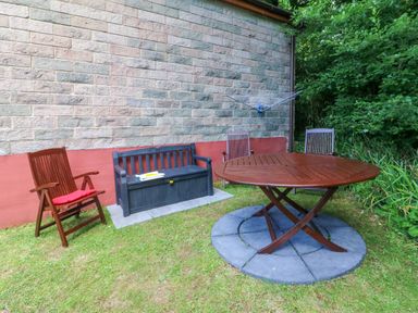 An outdoor seating area with wooden chairs a bench and a round wooden table on grass at 4 The Park in Kilkhampton