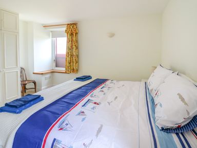 A bedroom with a bed with nautical themed bedding, folded towels, a window with floral curtains, a wooden chair, and built-in wardrobe at West Dairy near Newport Pembrokeshire