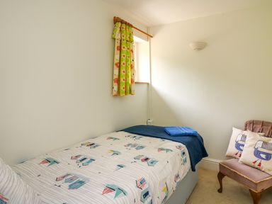 A bedroom with a single bed a chair with two cushions and a small window with curtains at West Dairy near Newport Pembrokeshire