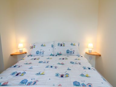 A bedroom with a bed featuring bedding with house and sailboat designs and two corner wall shelves with lamps at West Dairy near Newport Pembrokeshire