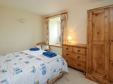 A bedroom with a bed towels a wooden dresser and wardrobe near a window at West Dairy near Newport Pembrokeshire