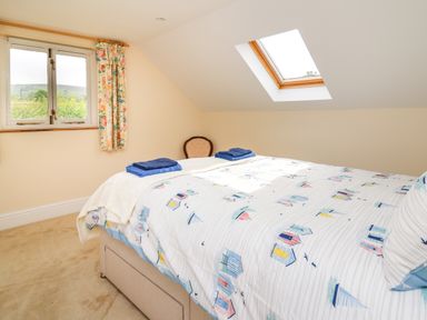 A bedroom with a bed with patterned bedding a chair a window with floral curtains and a skylight at West Dairy near Newport Pembrokeshire
