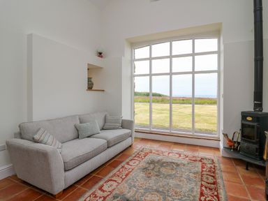 A living room with a sofa cushions rug stove and large window showing a garden view at West Dairy near Newport Pembrokeshire