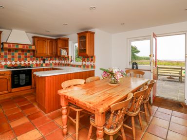 A kitchen and dining area with wooden table and chairs tiled floor and open door showing outdoor area at West Dairy near Newport Pembrokeshire