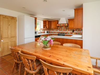 A kitchen with wooden cabinets a white refrigerator and a wooden dining table with chairs and flowers at West Dairy near Newport Pembrokeshire