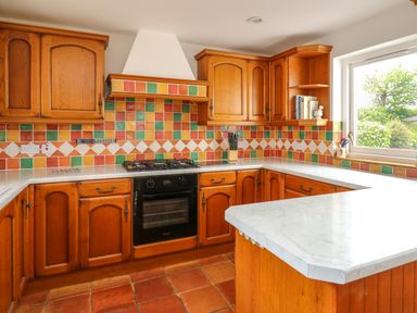 A kitchen with wooden cabinets tiled backsplash and a marble countertop at West Dairy near Newport Pembrokeshire