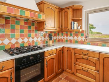 A kitchen corner with wooden cabinets a gas stove an oven colorful tiled backsplash and a window at West Dairy near Newport Pembrokeshire