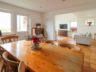 A dining area with wooden table and chairs with flower centerpiece next to a lounge with armchairs and television at West Dairy near Newport Pembrokeshire