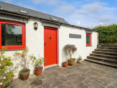 Exterior of a white cottage with red door and windows with flower pots near steps at West Dairy near Newport Pembrokeshire
