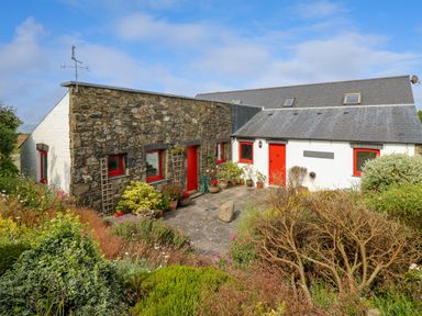 A stone and white house with red doors and windows surrounded by plants and shrubs at West Dairy near Newport Pembrokeshire