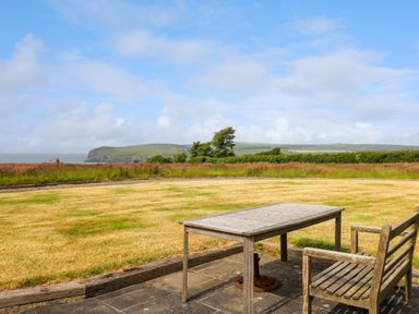 An outdoor patio with a wooden table and chair overlooking a grassy field and coastal landscape at West Dairy near Newport Pembrokeshire