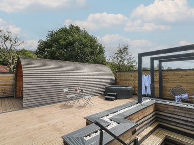 An outdoor wooden deck with a curved wooden cabin a small table and chairs a hot tub and a seating area at Paradise in Kenstone near Hodnet