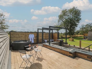 An outdoor deck with a hot tub two chairs and a table with dishes and glasses at Paradise Kenstone near Hodnet