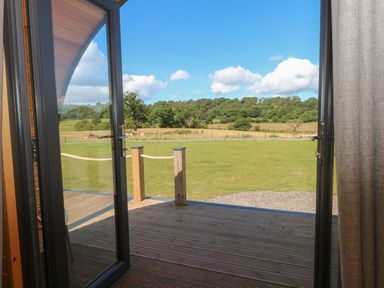 An open glass door leading to a wooden deck with a grassy field and trees in the background at Paradise in Kenstone near Hodnet