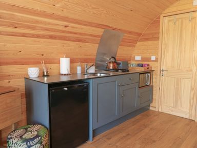 A kitchenette with grey cabinets a black mini fridge a kettle on the stove and wood panel walls at Paradise in Kenstone near Hodnet