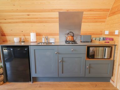 A kitchen with a black fridge gray cabinets a kettle on a stove a microwave and a tray with mugs at Paradise Kenstone near Hodnet