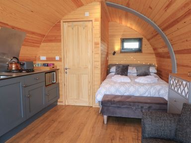 A small wooden cabin interior with a bed shower cabin kitchen area and a gray chair at Paradise in Kenstone near Hodnet