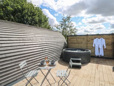 An outdoor deck with a hot tub two white robes hanging on a wooden fence and a small table with two chairs at Paradise in Kenstone near Hodnet