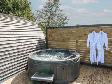 An outdoor hot tub with bubbling water and two white bathrobes hanging on a wooden fence at Paradise in Kenstone near Hodnet