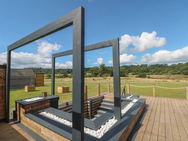 An outdoor wooden deck with stairs surrounded by wooden planters filled with white stones and large rectangular wooden frames in a grassy field at Paradise in Kenstone near Hodnet
