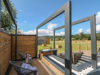 An outdoor wooden deck with two chairs a small table with drinks and a fenced grassy field at Paradise Kenstone near Hodnet