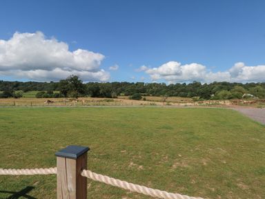 A grassy open field with a wooden post and rope fence under a blue sky at Paradise Kenstone near Hodnet