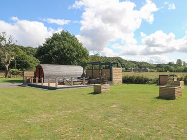 An outdoor area with a wooden pod structure and fenced deck surrounded by grass and trees at Paradise Kenstone near Hodnet