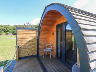 A wooden curved outdoor structure with glass doors and two chairs on a deck at Hawkstone Kenstone near Hodnet