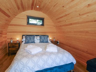 A bedroom with a bed with pillows and robes inside a wooden curved cabin at Hawkstone Kenstone near Hodnet