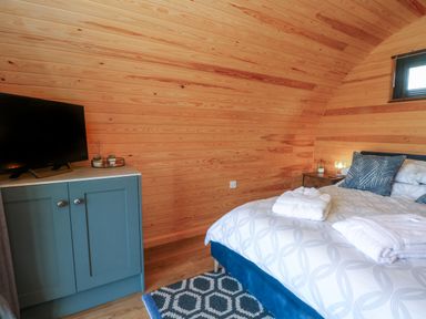 A bedroom with a blue cabinet holding a television and a bed with white linens and blue pillows at Hawkstone Kenstone near Hodnet