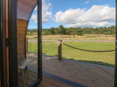 View through open glass door to a wooden deck with rope railing and green fields and trees in the background at Hawkstone Kenstone near Hodnet