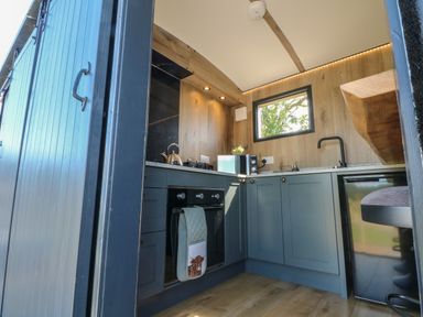 A modern kitchen with blue cabinets a black oven a microwave kettle and a window at Hawkstone Kenstone near Hodnet