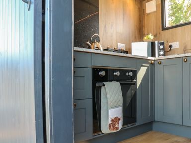 A kitchen with blue cabinets a kettle a microwave and an oven with oven gloves at Hawkstone Kenstone near Hodnet