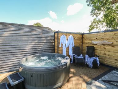 An outdoor area with a hot tub two lounge chairs with towels two white robes hanging on a wooden fence at Hawkstone Kenstone near Hodnet