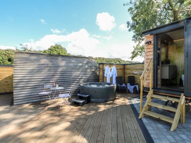 An outdoor wooden deck with a hot tub two chairs a small table and two white bathrobes at Hawkstone Kenstone near Hodnet
