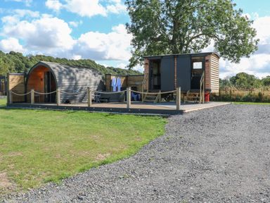 An outdoor area with a wooden pod and a small cabin on a deck with a hot tub and seating at Hawkstone Kenstone near Hodnet